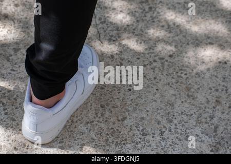 Sezione bassa, primo piano di una scarpa da ginnastica bianca che cammina sul marciapiede al Parque José Martí a Ciego de Ávila, Cuba – 21 agosto 2026 Foto Stock