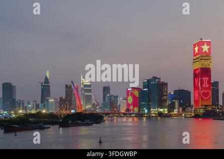 Una skyline densa illuminata con torri illuminati di rosso, un ponte ad arco e chiatte da carico accanto a un ampio fiume sotto un cielo notturno nebbioso. Foto Stock