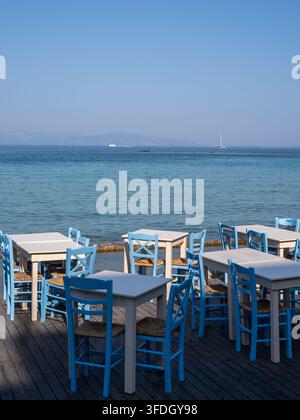 Tavoli e sedie blu e bianchi su una terrazza di ristorante sul lungomare con vista sul calmo mar Egeo Foto Stock