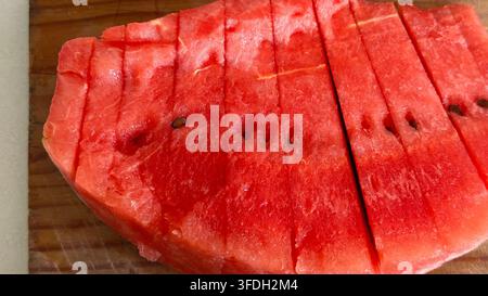 Anguria fresca tagliata in più fette su un tagliere di legno, che illustra la frutta estiva, la preparazione del cibo e gli spuntini salutari. Foto Stock
