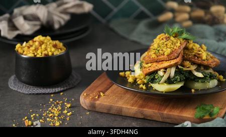 Un pasto gourmet a base vegetale con bistecche di tofu condite su un letto di verdure saltate e patate a fette. L'illuminazione laterale morbida evidenzia la c Foto Stock