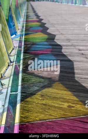 Vista dei pannelli di vetro colorati del Ponte Pedonal Pedro e Ines che proiettano ombre geometriche vibranti sul passaggio pedonale in legno a Coimbra, Coimbra, Por Foto Stock