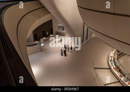 Vista dell'interno moderno del Museo Nazionale Zayed con pareti architettoniche curve, vetrine e visitatori che camminano attraverso la sala ad Abu Dhabi Foto Stock