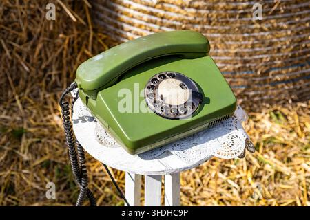Telefono verde vintage a disco visualizzato su un supporto di pizzo bianco con balle di paglia in un ambientazione esterna soleggiata. Foto Stock