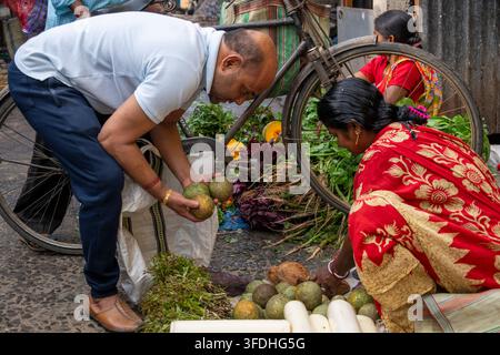 Un uomo seleziona della frutta da acquistare da una venditrice a uno stand di mercato all'aperto vivace pieno di prodotti freschi e una bicicletta Foto Stock