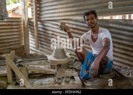 Un uomo mostra con orgoglio un vaso di argilla finito utilizzando l'argilla del Gange mentre lavora a un tornio tradizionale in un ambiente rurale Foto Stock