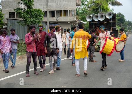 Giovani uomini coperti di polvere colorata ballano e suonano tamburi durante una vibrante celebrazione di strada del festival indù Holi Foto Stock