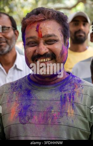 Un uomo con una vivace polvere Holi spalmata sul viso e sui vestiti splende di gioia, celebrando una tradizionale festa indiana Foto Stock