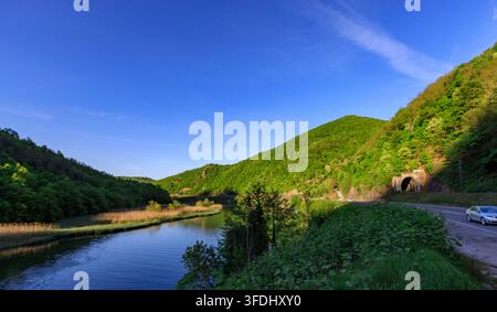 Bellissima catena montuosa con un fiume che la attraversa. Il cielo è sereno e azzurro, e il sole splende intensamente. La scena è tranquilla e serena Foto Stock