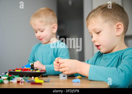 Due ragazzi che costruiscono con i blocchi, assemblano piccoli pezzi e si concentrano sulla costruzione. Seduti al tavolo a casa, gioco creativo, apprendimento e interazione tra fratelli Foto Stock