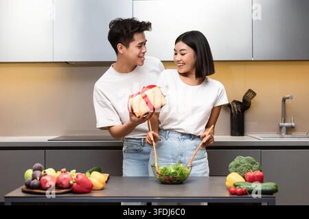 Amorevole marito cinese che dà moglie avvolto dono in piedi in cucina Foto Stock