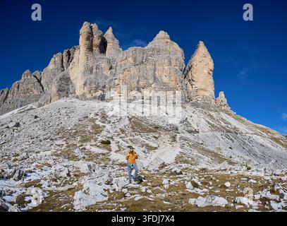 Alpinista donna posa sotto imponenti guglie di calcare nelle Dolomiti, Italia, con zaino e attrezzatura, enfatizzando la scala, l'esplorazione alpina, il turismo attivo, l'avventura all'aria aperta impegnativa Foto Stock