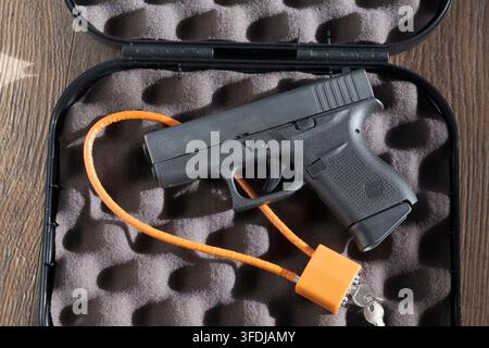 Una pistola semiautomatica Glock 43 riposa in una custodia rigida foderata in schiuma accanto a un blocco di innesco a cavo arancione non attaccato e chiavi, illustrando l'immagazzinamento delle armi da fuoco Foto Stock