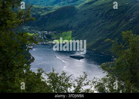 Prospettiva aerea di un profondo fiordo norvegese con una nave da crociera ancorata in acque blu scuro, affiancata da ripide pendici boschive e una valle verde. Foto Stock