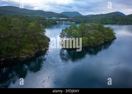 Prospettiva aerea di un fiordo norvegese che mostra isole ricoperte di foreste di conifere, acqua blu-verde profonda, montagne lontane e una crociera Foto Stock