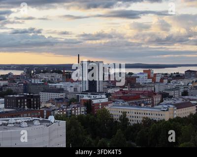 Vista aerea del paesaggio urbano di Tampere con moderni grattacieli, architettura storica in mattoni e alberi verdi rigogliosi sotto un cielo di tramonto soffice Foto Stock