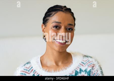 Donna afroamericana che sorride calorosamente indossando un maglione di lana morbido nell'angolo dello studio Foto Stock