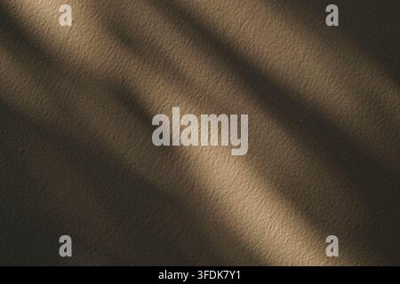 Raggi di sole caldi e ombre diagonali si proiettano su una superficie murale beige strutturata, creando uno sfondo architettonico minimalista. Foto Stock