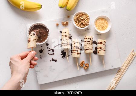 Donna immerso lecci di banana con noci spruzzano. Cucinare dolci fatti in casa per vegan o bambini. Vista dall'alto. Foto Stock