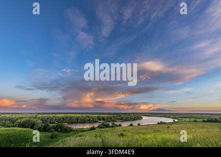 La luce dorata si riversa sulla curva gentile del fiume. Il cielo dipinge tonalità di rosa, viola e blu Foto Stock