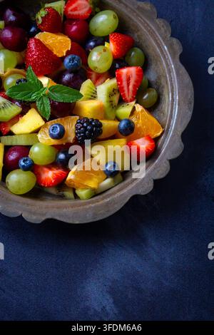 Insalata di frutta mista fresca con fragole, mirtilli, kiwi e uva in una ciotola rustica Foto Stock