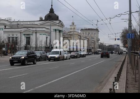 Le auto viaggiano su una strada trafficata in città. Gli edifici alti fiancheggiano la strada e il cielo è nuvoloso. È una giornata normale con un flusso di traffico regolare. C Foto Stock