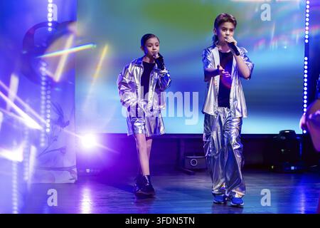 Cantante ragazza e ragazzo che si esibiscono con microfono sul palco. Duo di bambini in abito argentato a un concerto musicale. Evento di talent show con faretto e col Foto Stock