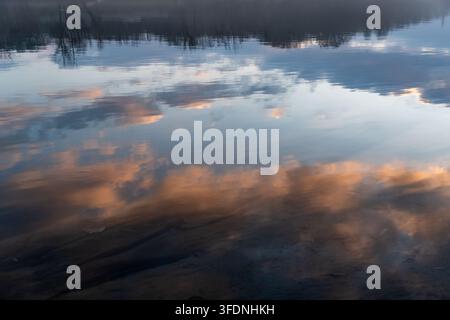 Sfondo di natura autunnale sereno con morbide nuvole arancioni che si riflettono sulle onde d'acqua tranquille al crepuscolo, creando un'atmosfera sognante e pacifica Foto Stock