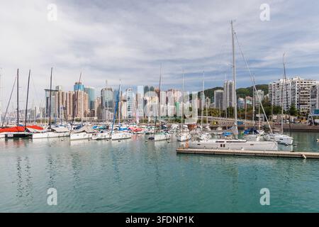 Hong Kong, Cina – 27 novembre 2025: Yacht di lusso ormeggiati in una marina con lo skyline di Hong Kong Island e Victoria Harbour sullo sfondo. Foto Stock