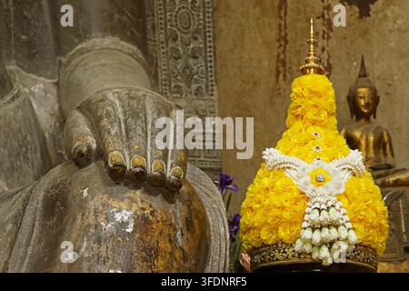 Primo piano di una mano di Buddha antica in pietra appoggiata sul ginocchio con un piedistallo tradizionale per offerte floreali al Wat Na Phra Meru, Ayutthaya Foto Stock