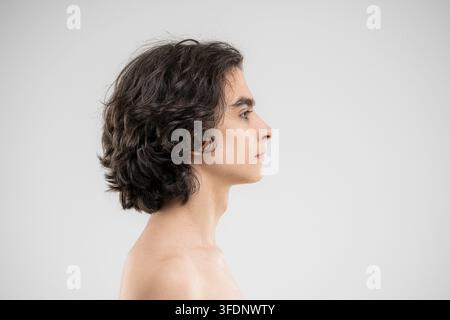 Profilo di un giovane uomo affascinante con capelli ricci folti su sfondo bianco Foto Stock
