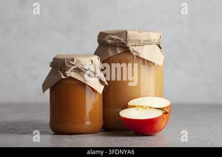 Due barattoli di marmellata di mele con mezza mela su sfondo grigio. Cibo biologico fatto in casa Foto Stock