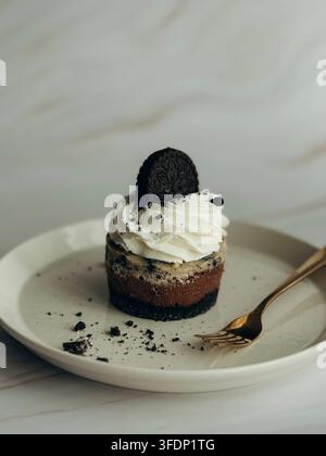 Mini cheesecake Oreo con panna montata su piatto di ceramica con forchetta dorata, vista ad angolo alto Foto Stock