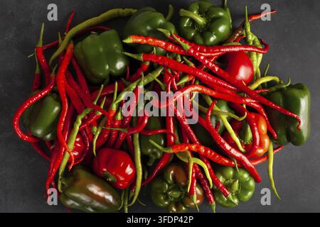 Vista dall'alto di peperoncini freschi assortiti e peperoni verdi e rossi su sfondo scuro, perfetti per la cucina piccante e i temi del cibo organico Foto Stock