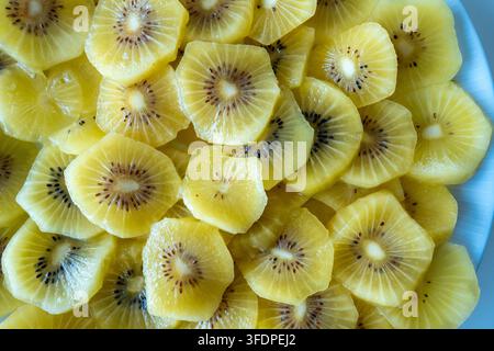 Primo piano luminoso di fette di kiwi dorate disposte su un piatto, che mostrano la polpa gialla succosa, i semini e la consistenza fresca. Spuntino o brea sano e vivace Foto Stock