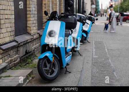 Monopattini elettrici blu e bianchi di un servizio di sharing allineati su un marciapiede di ciottoli, un nuovo strato di trasporto caduto in una strada secolare. Foto Stock
