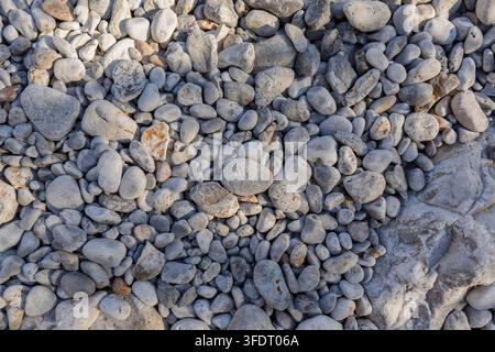 Primo piano di molti ciottoli lisci e arrotondati e piccole rocce sparse sulla spiaggia, visti dall'alto. Sfondo astratto naturale di viaggio, vacanza ed estate Foto Stock