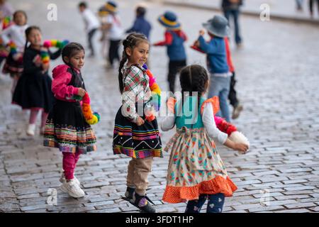 Un gruppo di bambini sorridenti in colorati costumi tradizionali andini danza e gioca su strade di ciottoli durante un vivace festival a Cusco, Perù, cap Foto Stock