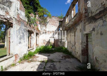 Una vista diurna dell'interno di una rovina di edificio abbandonato e senza tetto. La struttura presenta muri sgretolati con mattoni rossi esposti e vernice bianca s Foto Stock