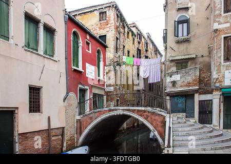 Ponte in pietra su un canale stretto con case residenziali colorate e biancheria appesa ad asciugare nel quartiere di Santa Croce, Venezia, Italia. Scena urbana Foto Stock