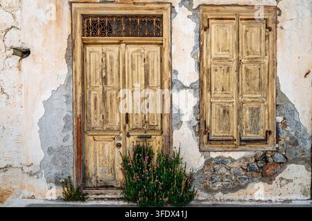 Primo piano di una porta di legno invecchiata e di una finestra su una facciata di casa tradizionale consumata in un villaggio cretese Foto Stock