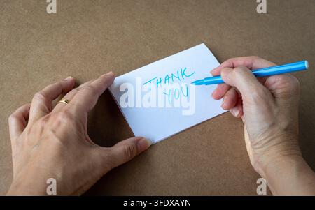 Donna che scrive una carta di ringraziamento con un pennarello blu. Vista ravvicinata. Foto Stock