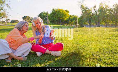 Donne anziane che godono di musica e tecnologia nel parco Foto Stock