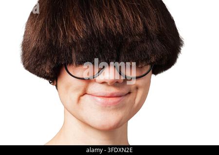 Una persona con un taglio di capelli a ciuffo marrone scuro distintivo e occhiali dalla montatura spessa mostra un sorriso sottile e giocoso, che suggerisce malizia o divertimento Foto Stock