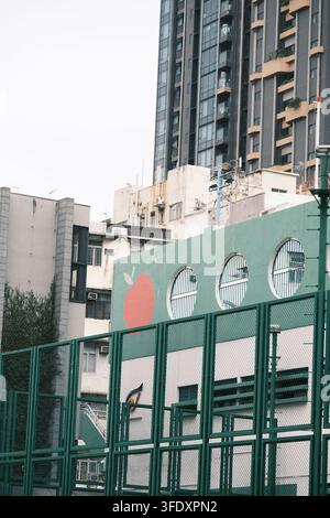 Le pareti verdi del mercato di To Kwa Wan hanno finestre rotonde, che contrastano nettamente con gli edifici vecchi e nuovi dietro di esse. Foto Stock