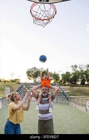 Famiglia multigenerazionale che gioca a basket all'aperto godendosi il tempo libero Foto Stock