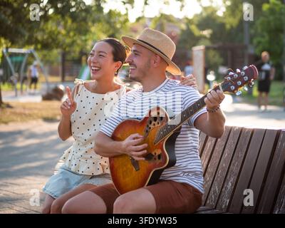 Momento romantico all'aperto mentre un uomo canta per la sua compagna con una chitarra acustica Foto Stock