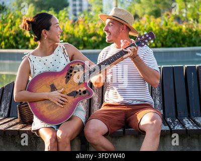 Donna allegra che prova la chitarra mentre il suo partner sorridente le mostra come suonare Foto Stock