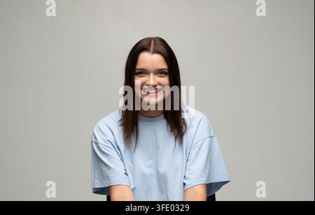 Giovane donna con capelli castani che sorride ampiamente, si sente positiva e felice in un ritratto da studio Foto Stock