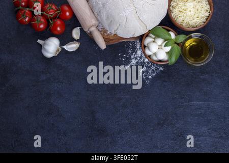 Ingredienti per la pizza margherita impasto crudo pomodorini basilico olio d'oliva mozzarella su tavolo di pietra scuro in cucina Foto Stock